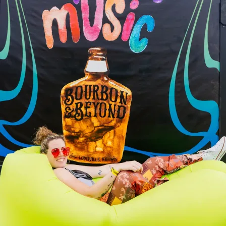 A fan relaxing on an inflatable in front of a painted Bourbon & Beyond mural