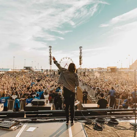 A performer on stage facing a huge daytime crowd at Welcome To Rockville