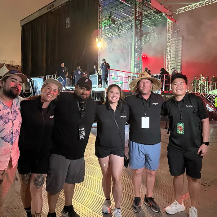 Six Jampack staff in branded shirts and event laminates standing in front of a festival stage during load-in