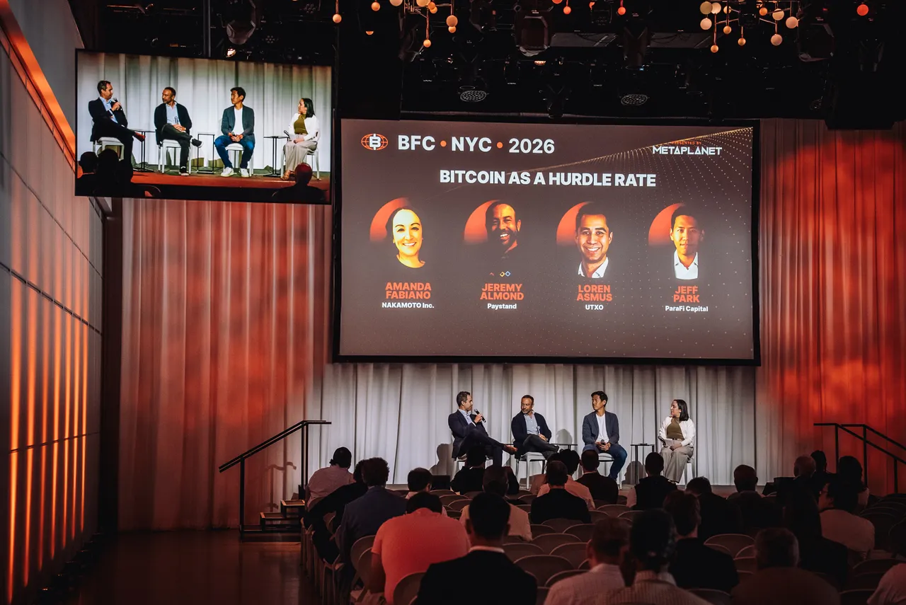 A panel session at the Bitcoin 2026 Symposium in New York — four speakers on stage, a full seated audience, and the session title on the screen behind them.